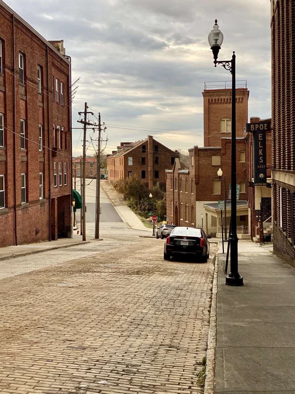 A cobblestone street running downhill between brick buildings in downtown Danville, with an ornate street lamp and the Elks lodge sign.