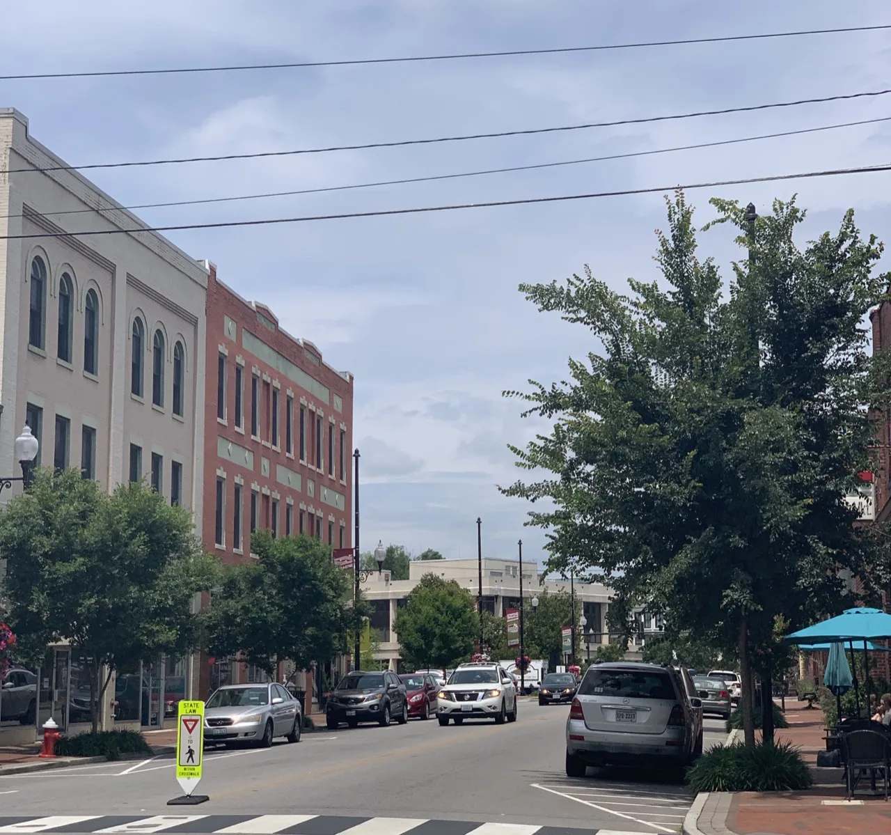 Craghead Street in Danville's River District — a brick commercial block with street trees, parked cars and a sidewalk cafe umbrella.
