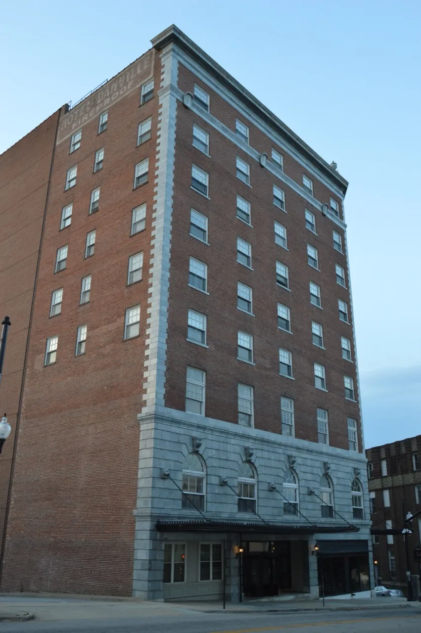 The 1927 Hotel Danville tower at dusk, its brick and granite facade lit against a deep blue evening sky.