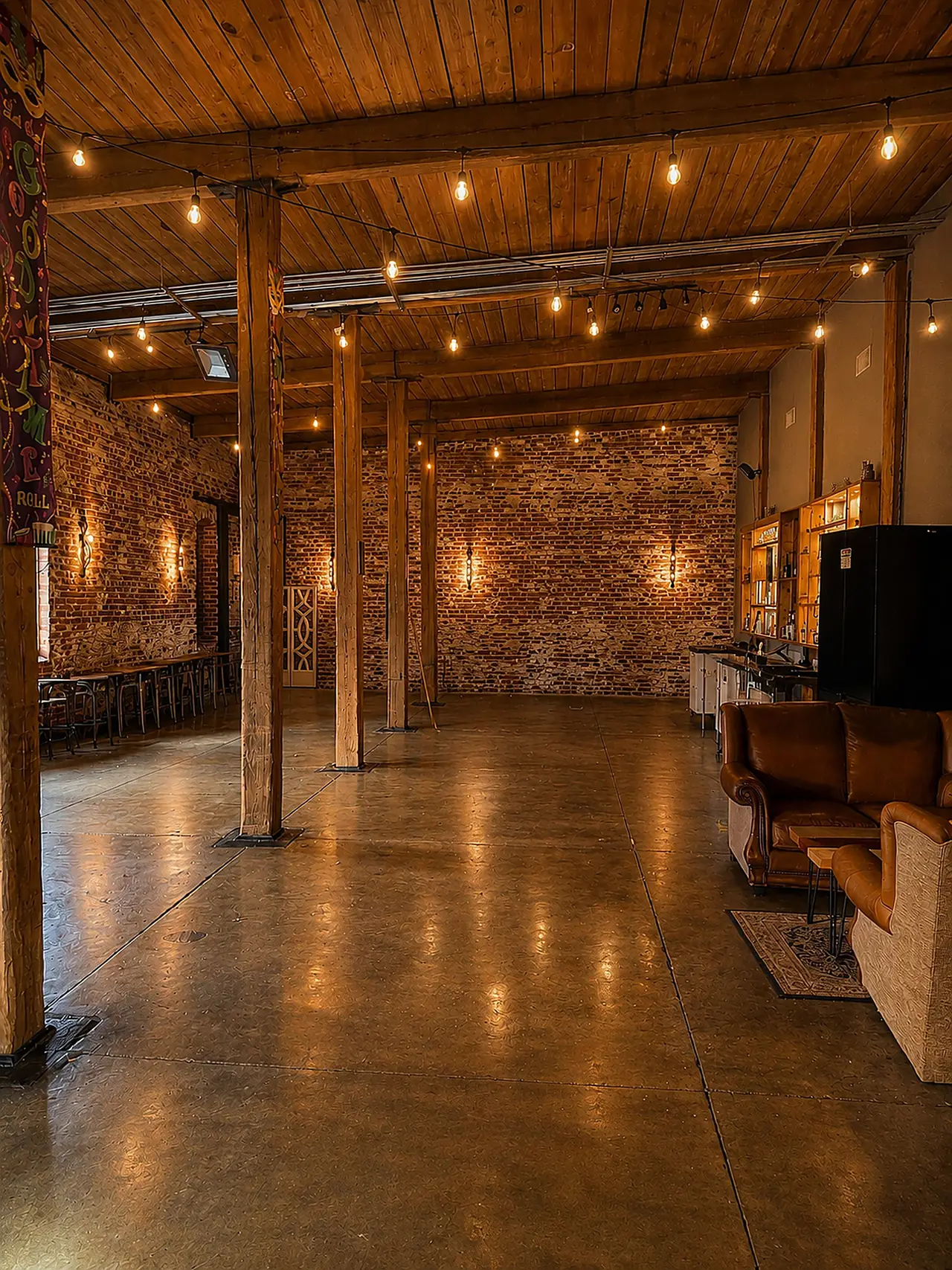 Flexible lounge and performance area with Edison string lights, exposed brick and a stage wall.