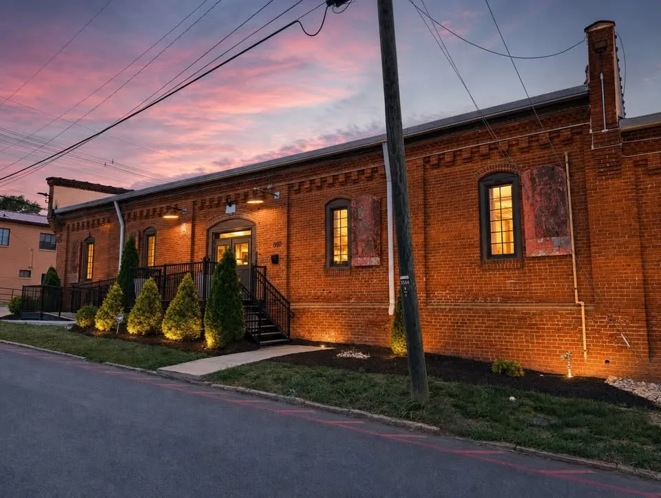 The front of Suite J at dusk — historic brick, glowing arched windows and railed steps up to the entrance at 680 Lynn Street.